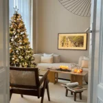 A cozy living room with a decorated Christmas tree, lit candles on a coffee table, modern furniture, and framed art on a beige wall, perfect for inspiring Christmas living room decor ideas for small spaces.