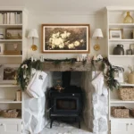 Farmhouse winter living room with a whitewashed stone fireplace, wood stove, evergreen garland, woven baskets, and neutral holiday accents